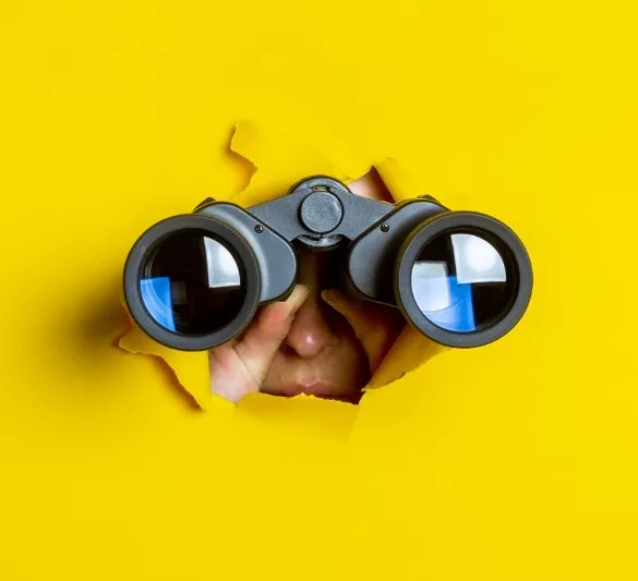 persona con binoculares atravesando una pared amarilla