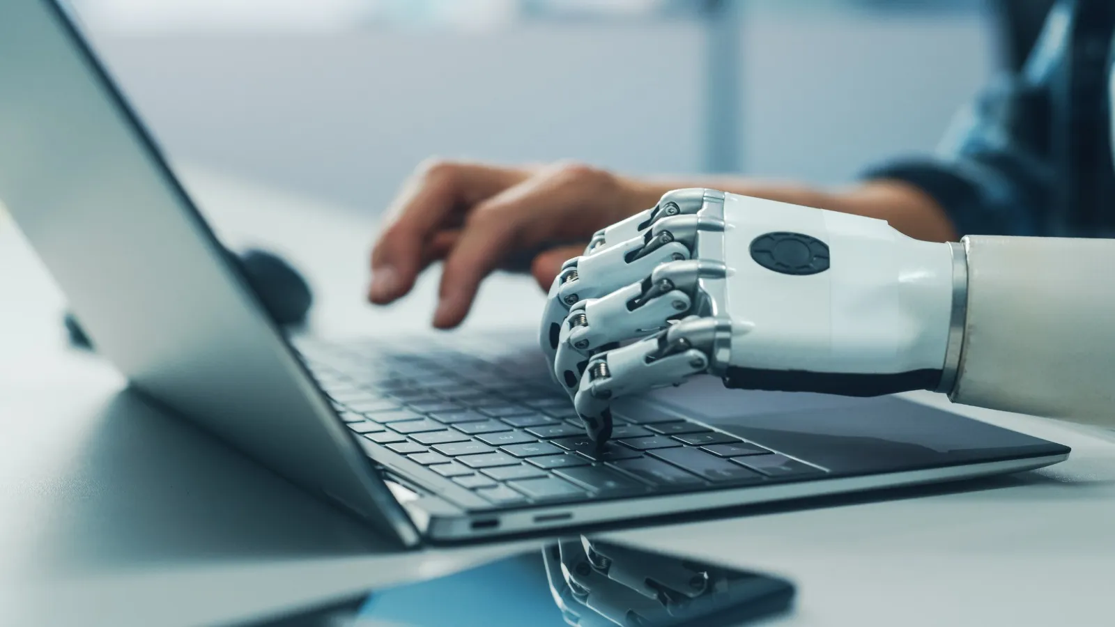 persona tecleando en un computador, una de sus manos es robótica